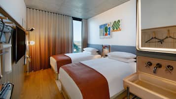 A hotel room with two beds, a large mirror, a TV, and a view of the city.