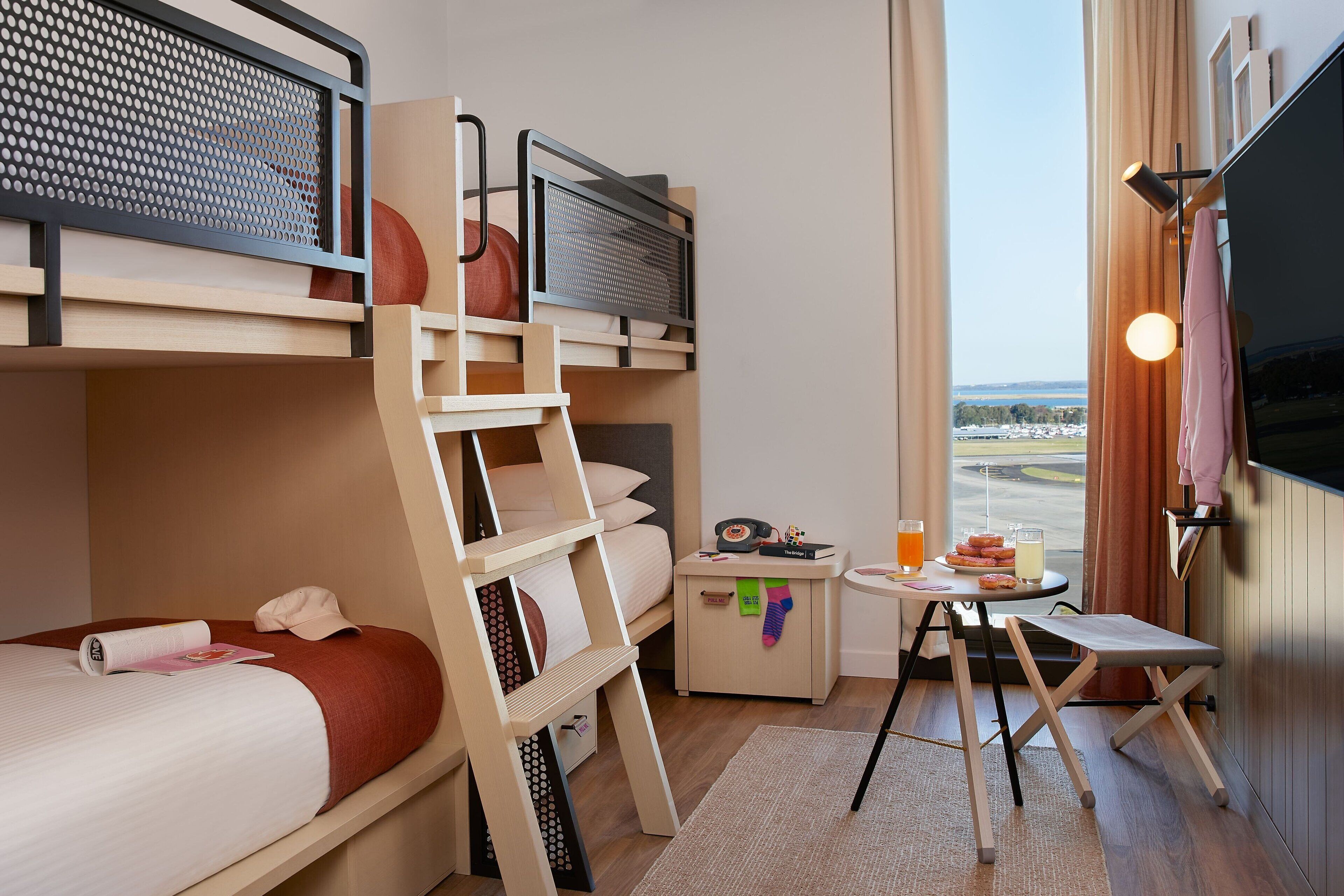 A hotel room with bunk beds, a small table with a drink, and a TV.
