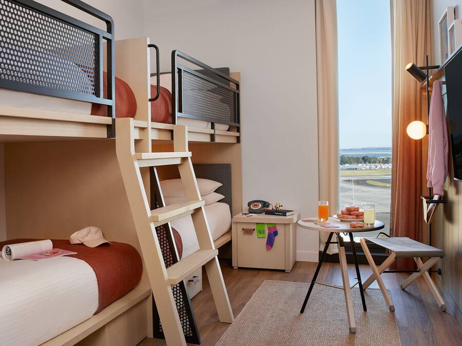 A hotel room with bunk beds, a small table with a drink, and a TV.