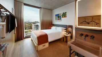 A hotel room with a bed, a TV, a bathroom with a sink, and a view of the city.
