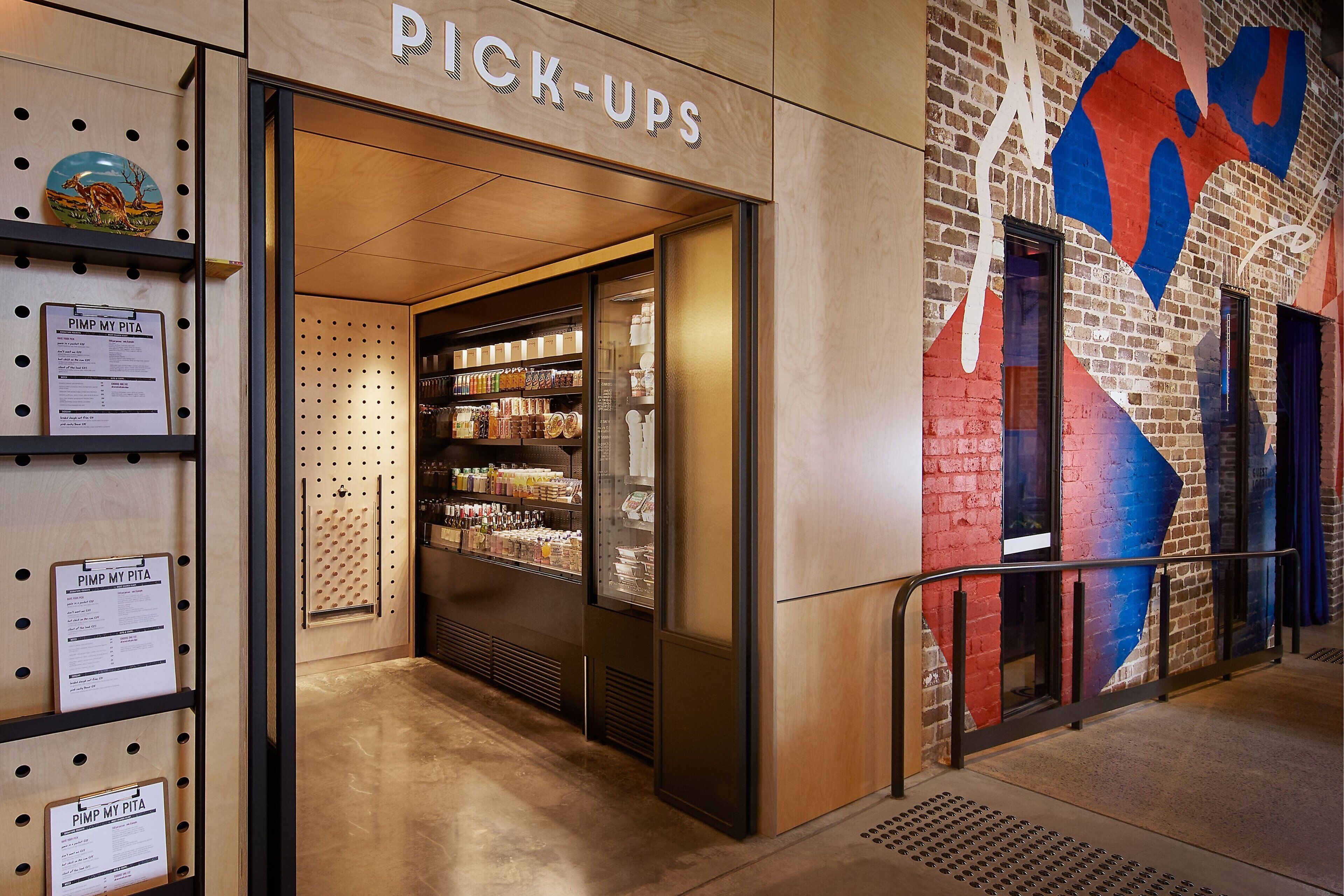 A store named 'PICK-UPS' with a glass door, shelves with various items, and a wall with a colorful abstract design.