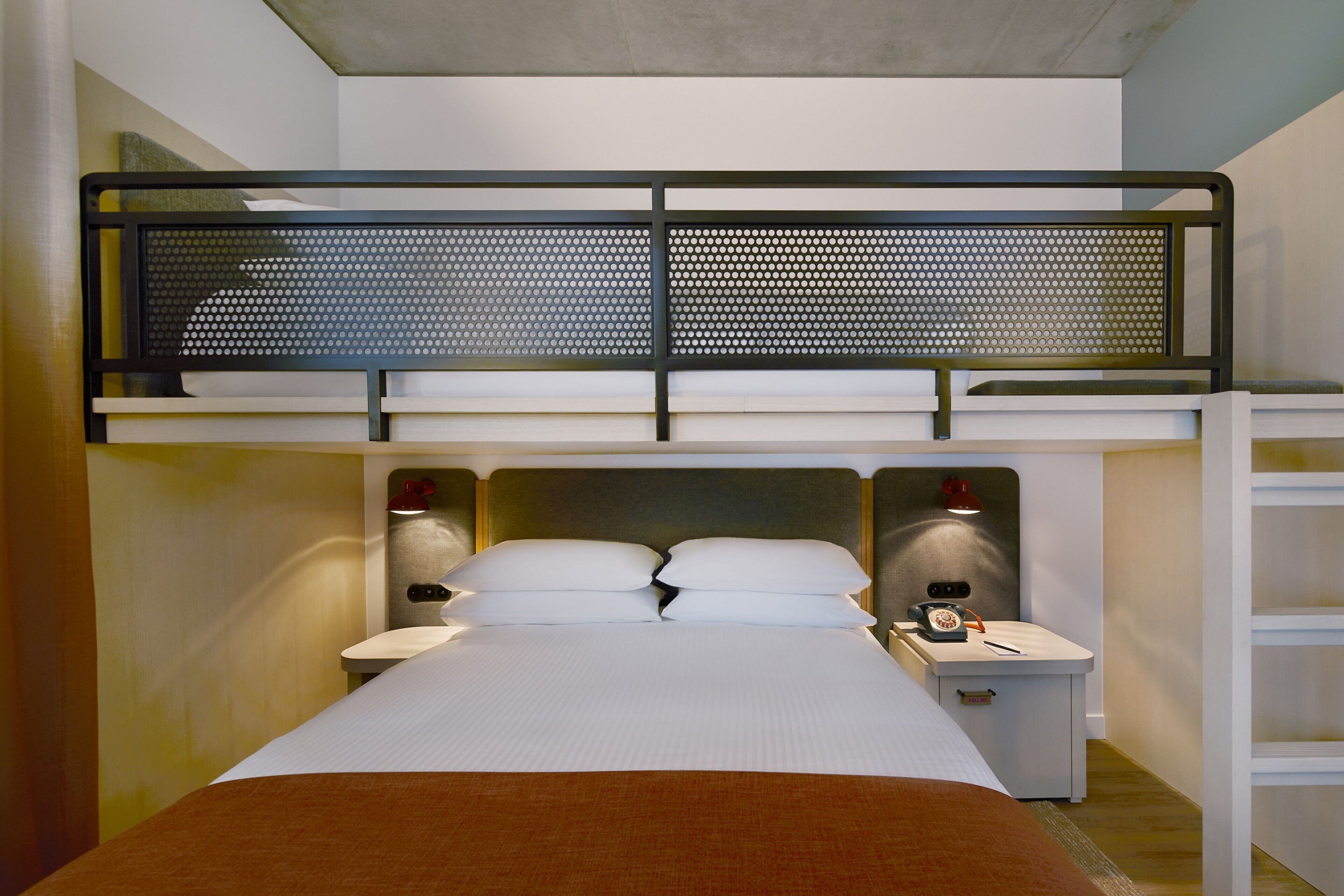 A hotel room with a bunk bed, a desk with a telephone, and a nightstand with a lamp.
