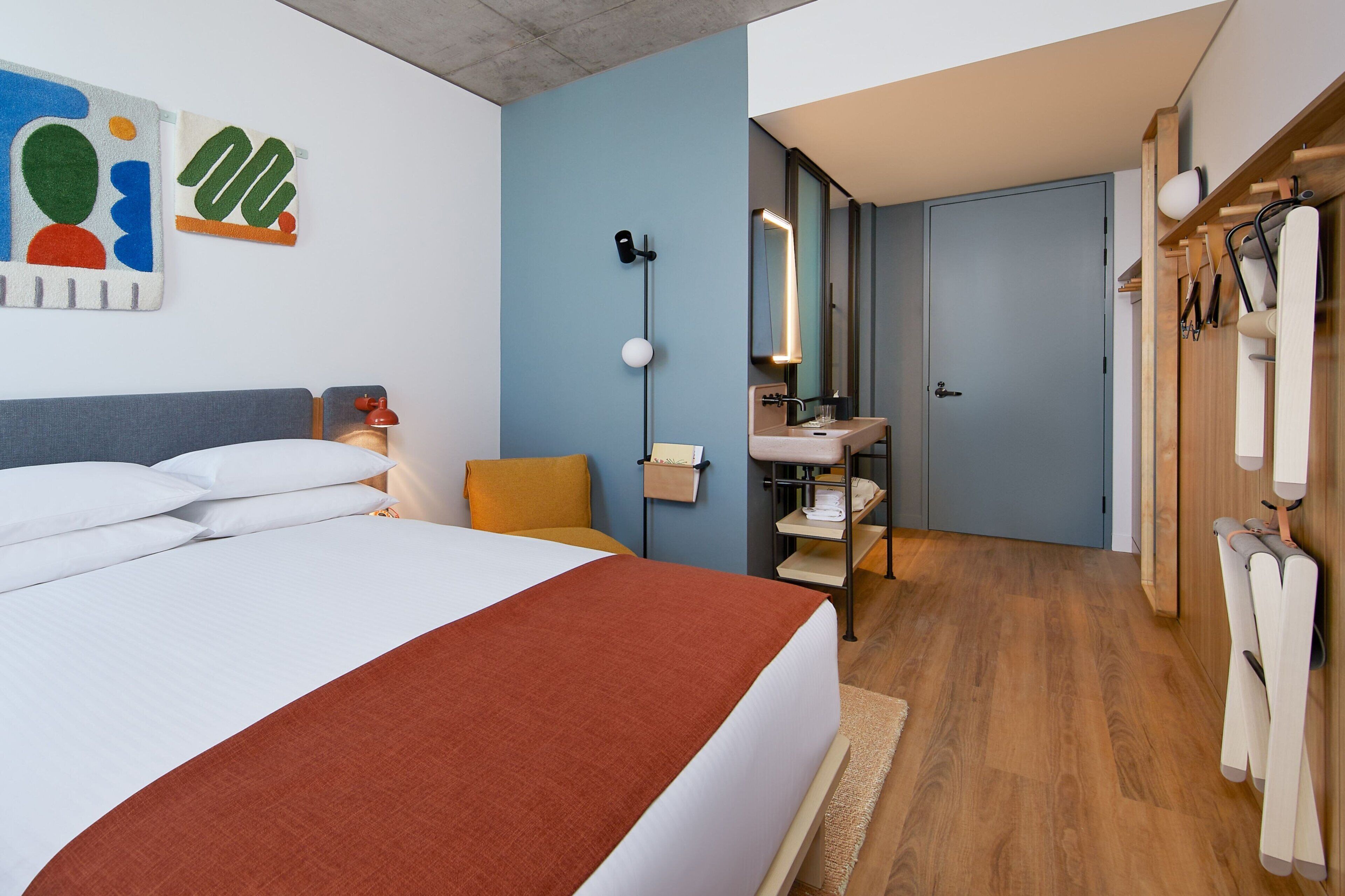 Una habitación de hotel moderna con una cama grande, un baño con espejo y lavamanos, y un armario de madera.