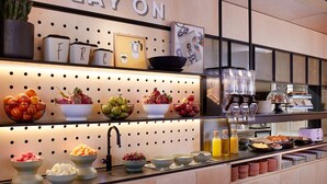 A buffet area with various food items and a 'PLAY ON' sign above. - Moxy Sydney Airport (Mascot)