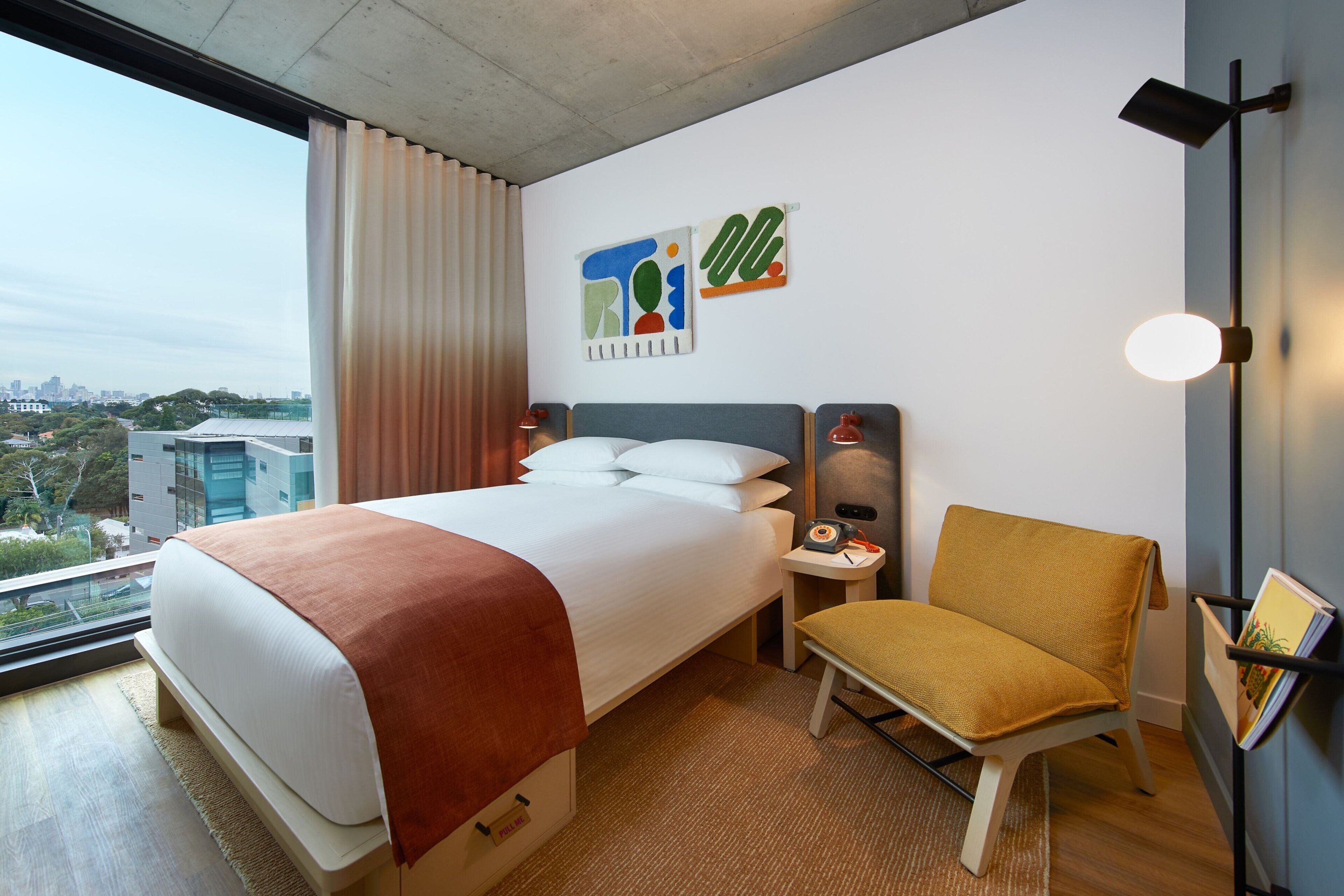Una camera d'albergo con un letto grande, una sedia, un comodino, una lampada e opere d'arte alle pareti.