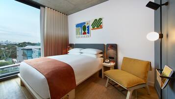 Una camera d'albergo con un letto grande, una sedia, un comodino, una lampada e opere d'arte alle pareti.