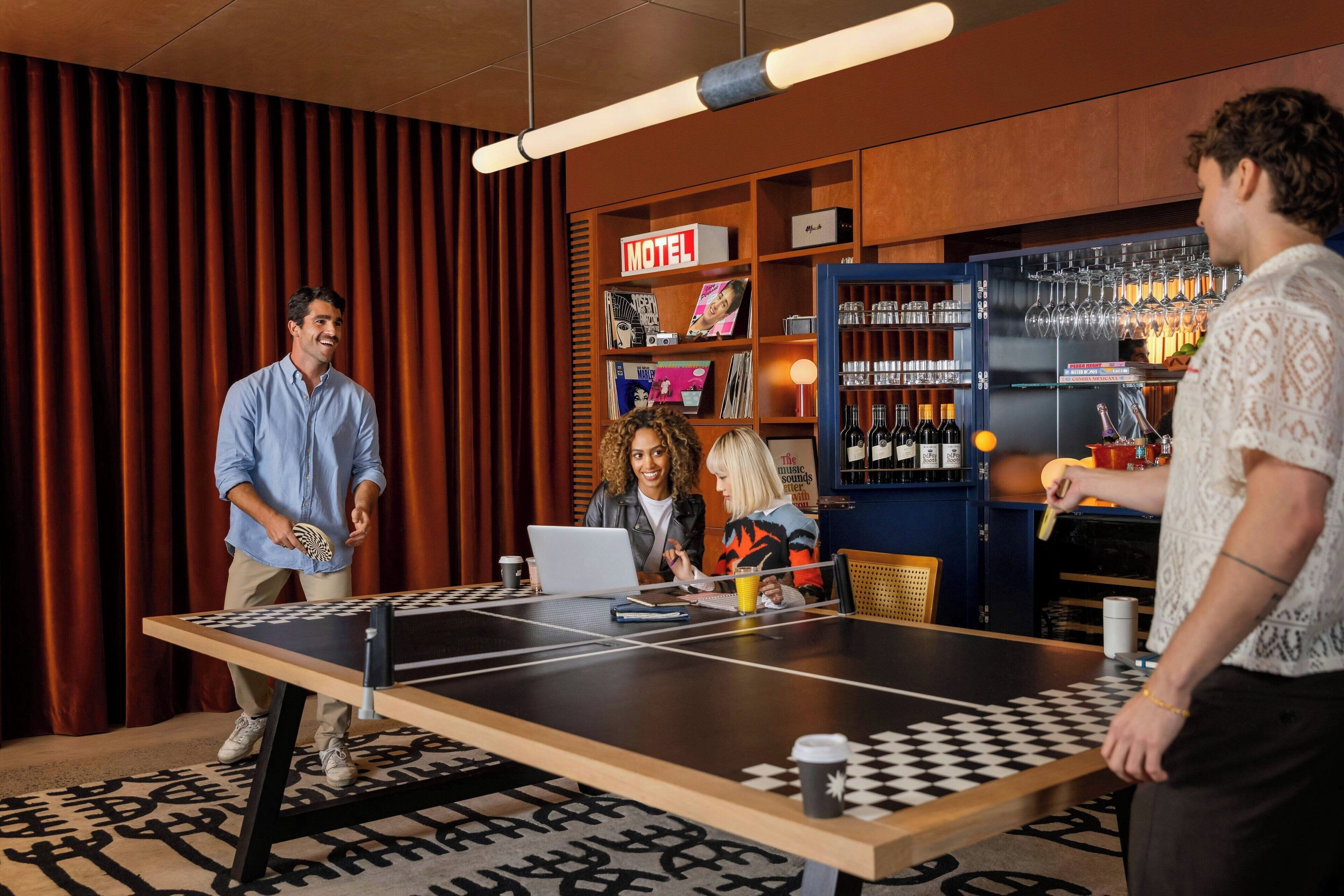A room with a ping pong table, a laptop, and a person playing. There is a bar area with bottles and glasses.