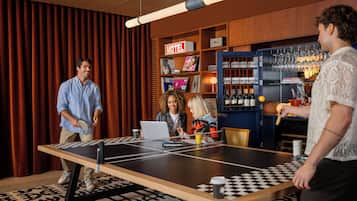 A room with a ping pong table, a laptop, and a person playing. There is a bar area with bottles and glasses.