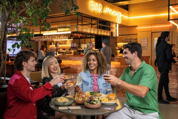 A group of people dining at a restaurant with a bar in the background. - Moxy Sydney Airport (Mascot)