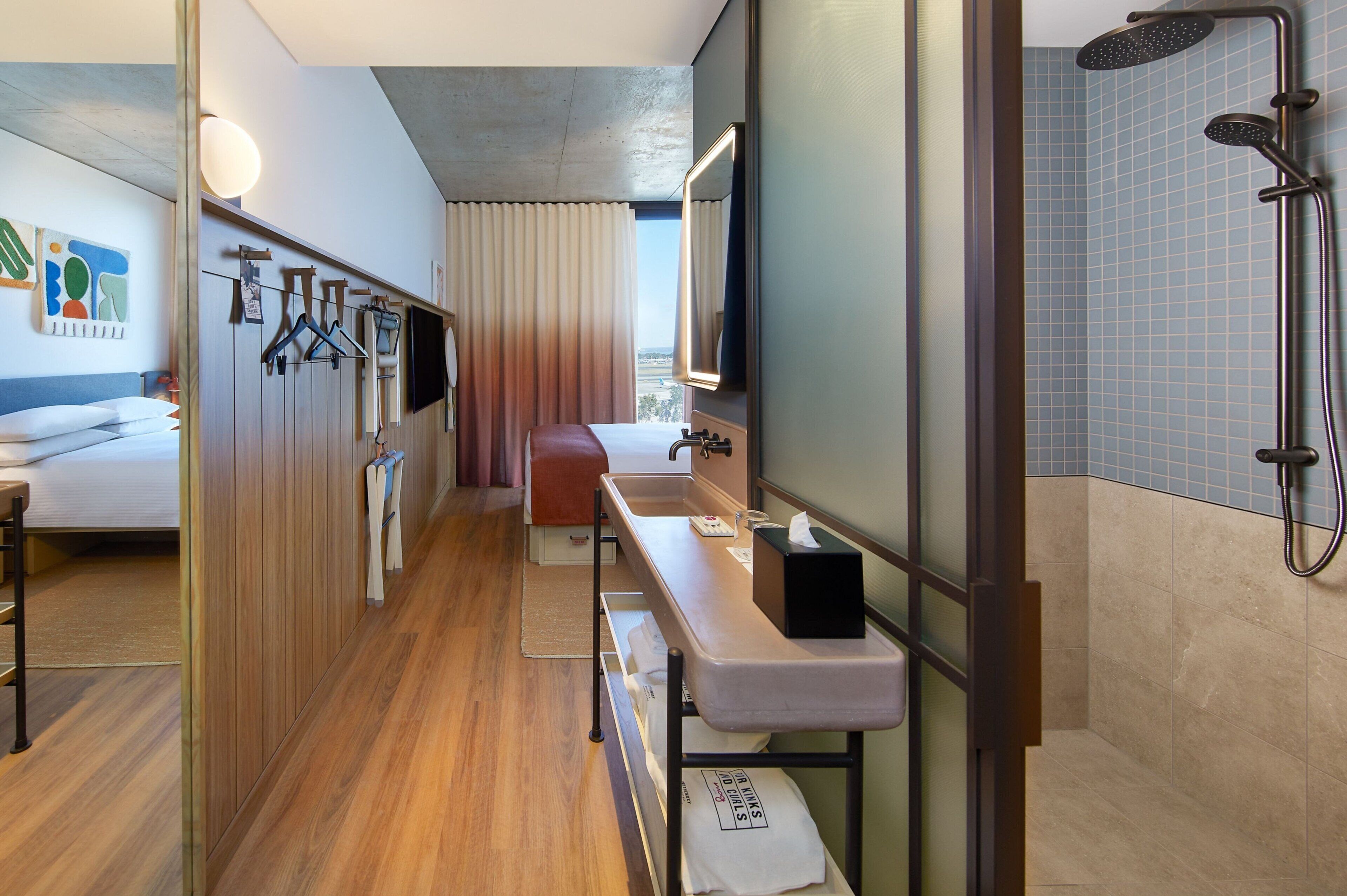 A hotel room with a bed, a desk, a shower, and a view of the city.