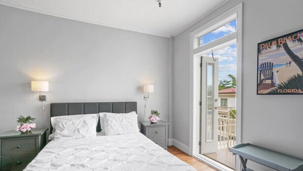 Ein Schlafzimmer mit Bett, Nachttischen, Fenster und einer Tür, die auf einen Balkon führt.