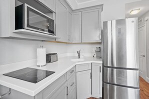 A modern kitchen with white cabinetry, a stainless steel refrigerator, a microwave, a toaster, and an induction cooktop. - Bijou Terrace Orchid-PALM BEACH (Palm Beach)