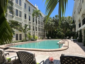 A swimming pool with lounge chairs and palm trees, surrounded by a building with multiple windows and balconies. - Bijou Terrace Orchid-PALM BEACH (Palm Beach)
