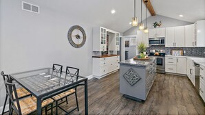 Une cuisine moderne avec des meubles blancs, un îlot central et un coin repas doté d’une table à plateau en verre.