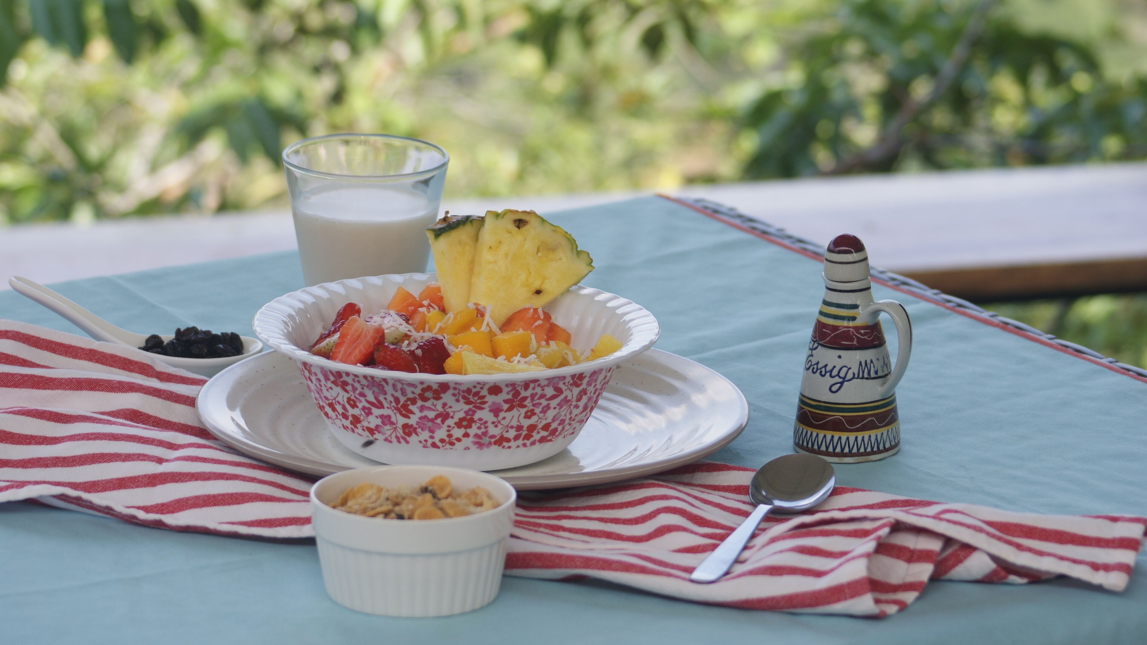 A table with a bowl of fruit salad, a glass of milk, a small bowl of cereal, a sugar bowl, and a decorative pitcher.
