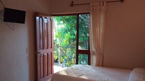 A room with two beds, a ceiling fan, a TV mounted on the wall, and a window with curtains. - Casa Mamá Maya   (Puerto Escondido)