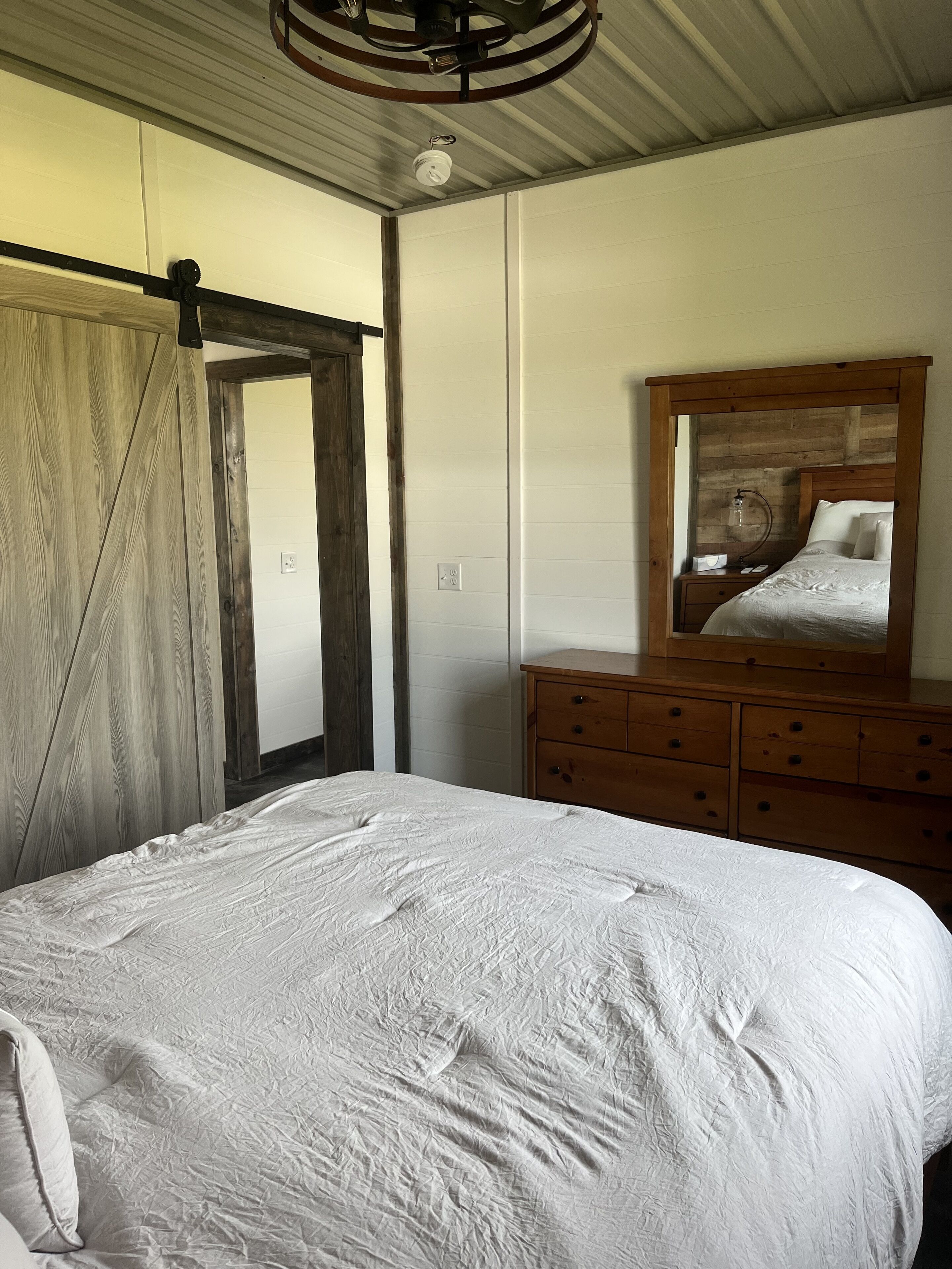 A bedroom with a bed, wooden dresser, and a mirror.