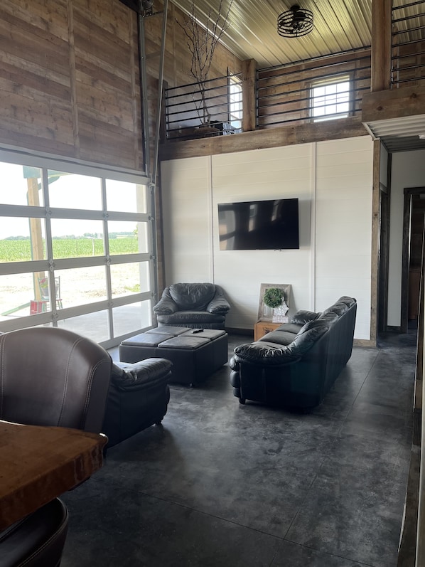 A spacious living area with a large window, a flat-screen TV mounted on the wall, and leather sofas.