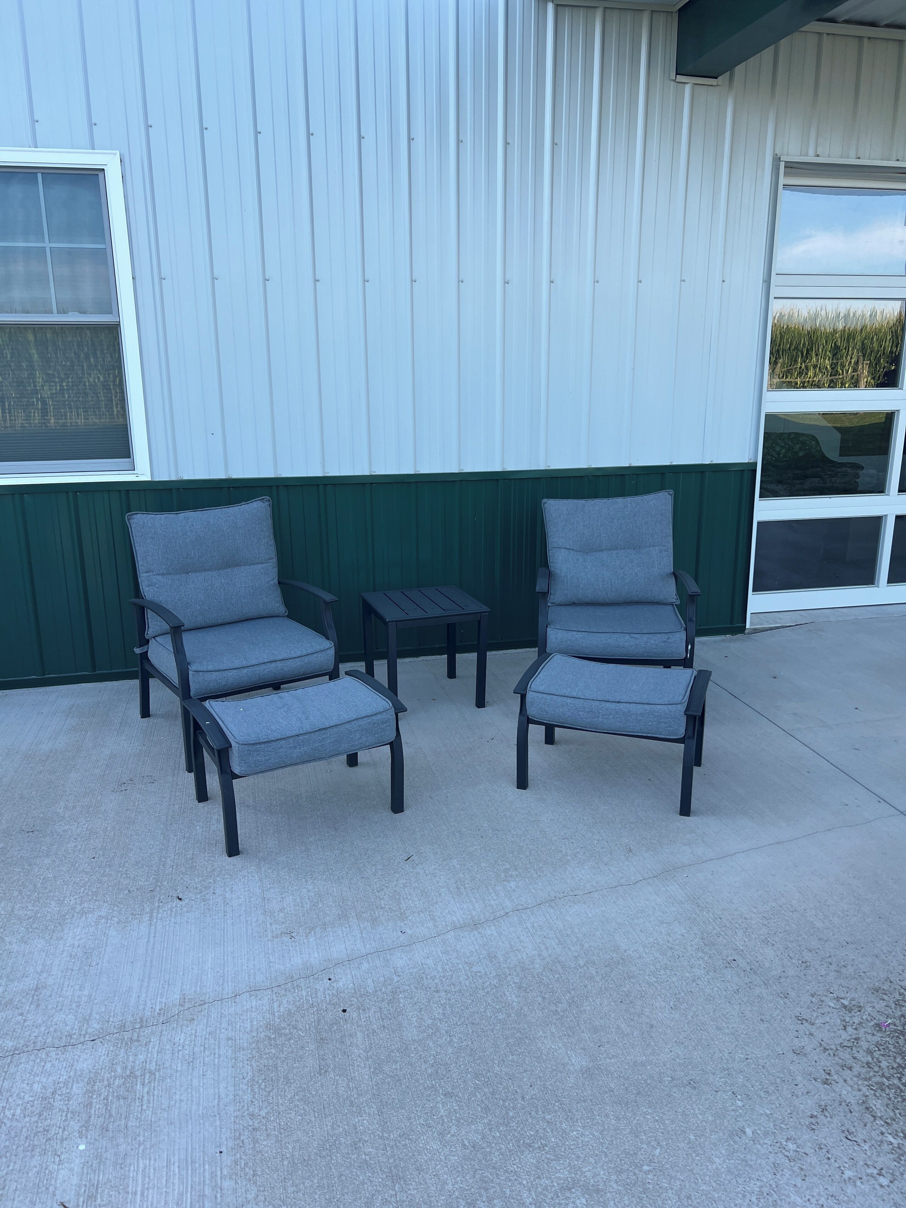 Two grey lounge chairs and a small table outside a building with a green and white exterior.