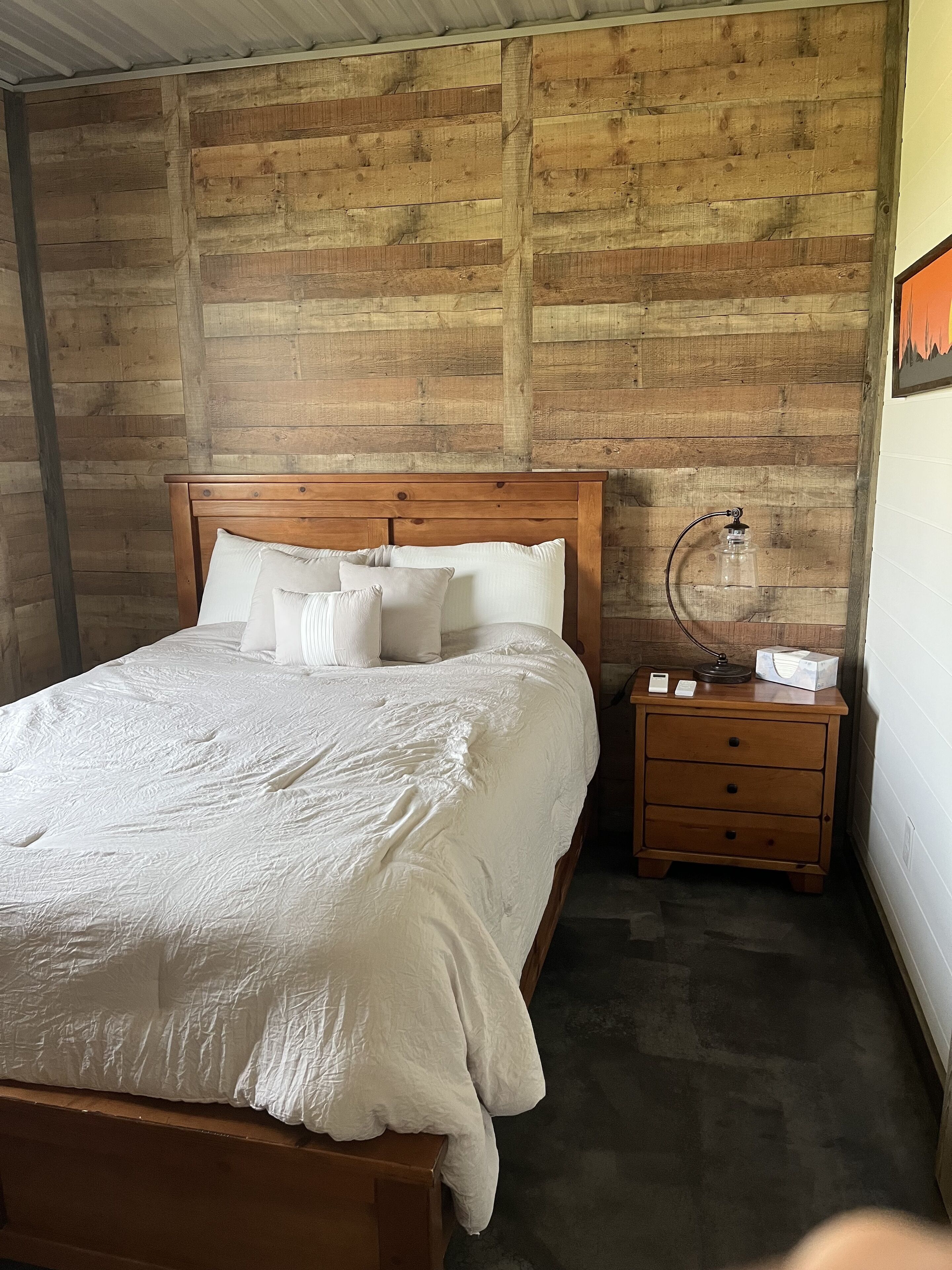 Une chambre à coucher avec une tête de lit en bois, un couvre-lit blanc et une table de chevet sur laquelle se trouvent une lampe et une boîte de mouchoirs.