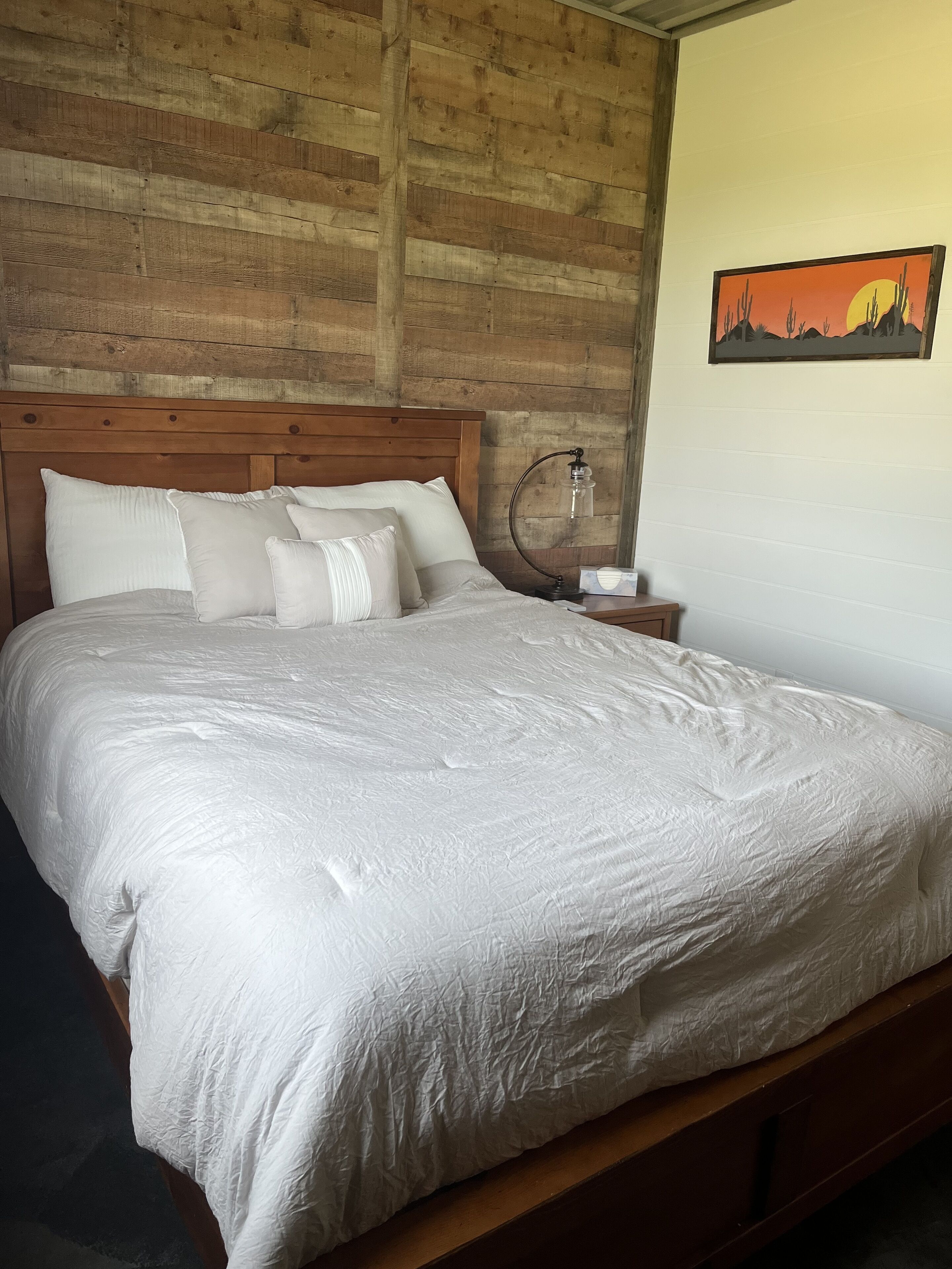 Una cama con cabecera de madera, ropa de cama blanca y una mesita de noche con lámpara.