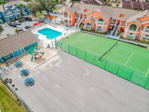 An aerial view of a hotel with a swimming pool, tennis court, and outdoor seating area.