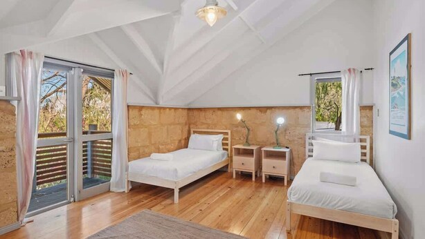 Une chambre avec deux lits, un plancher en bois, un ventilateur de plafond et une vue sur l’extérieur, accessible par une porte coulissante.