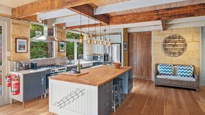 Une cuisine moderne avec un îlot central, des poutres en bois, des luminaires suspendus et une grande horloge au mur.