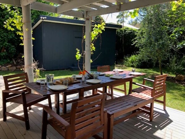 An outdoor wooden deck with a table set for dining, surrounded by chairs.