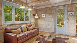 Une pièce avec un canapé en cuir, une table basse en bois, un tapis en peau de vache, un mur en pierre et une porte donnant sur l’extérieur.