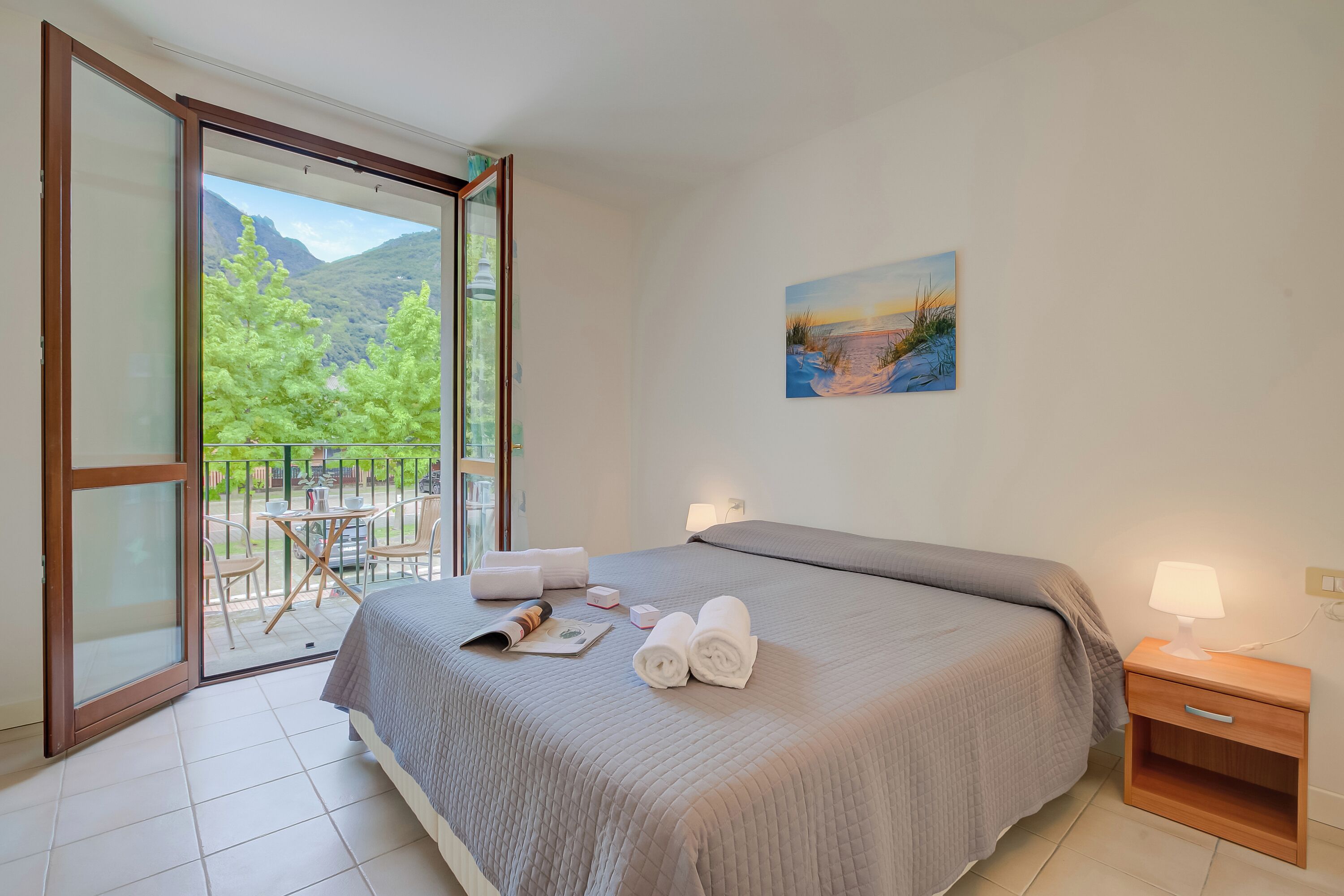 Ein Schlafzimmer mit Bett, Nachttisch, einem Gemälde und einem Balkon mit Stühlen und Tisch.