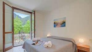 A bedroom with a bed, a nightstand, a painting, and a balcony with chairs and a table. - Porto Letizia Napoli 4, Porlezza, Italy (Porlezza)