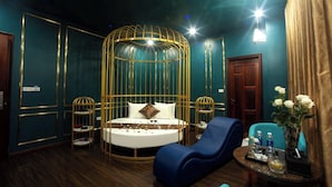 Ein luxuriöses Zimmer mit einem runden Bett, einem blauen Lounge-Sessel, einem kleinen Tisch mit Blumenvase und einer Holztür.
