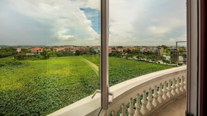 Ein Balkon mit Blick auf ein grünes Feld und Gebäude mit roten Dächern in der Ferne.