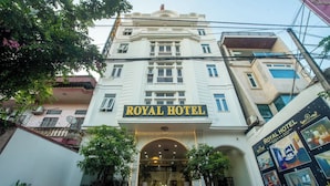 Ein Gebäude mit einem Schild, auf dem „ROYAL HOTEL“ steht, am Eingang. Es zeigt eine Treppe mit Beleuchtung, Blumentöpfen und einen klaren Blick ins Innere.