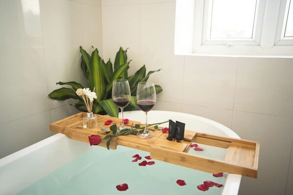 Una bañera con pétalos de rosa y dos copas de vino tinto sobre una bandeja de madera.