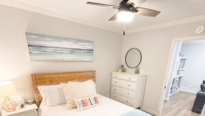 Un dormitorio con cama, mesitas de noche, ventilador de techo, espejo de pared y un cuadro.