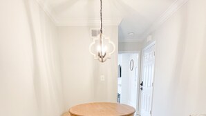 Una cocina con una mesa redonda de madera, armarios blancos y una lámpara colgante.