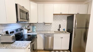 Una cocina moderna con armarios blancos, electrodomésticos de acero inoxidable, microondas, tostadora, lavavajillas y refrigerador.