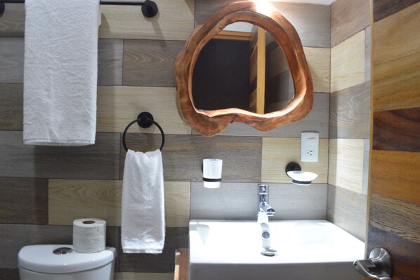 Un baño con tocador de madera, lavamanos, espejo y toallero.