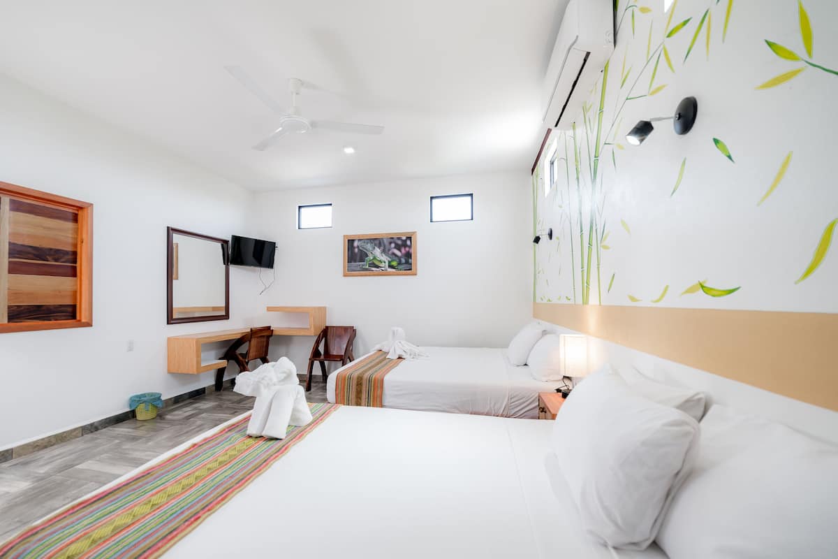 Une chambre d’hôtel avec deux lits, un bureau, une chaise, une télévision et un mur décoré de motifs de feuilles de bambou.