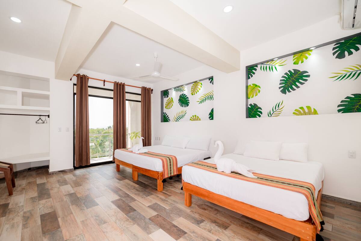 Une chambre d’hôtel avec deux lits, un ventilateur de plafond, une grande fenêtre avec des rideaux et un mur orné d’un motif de feuilles.