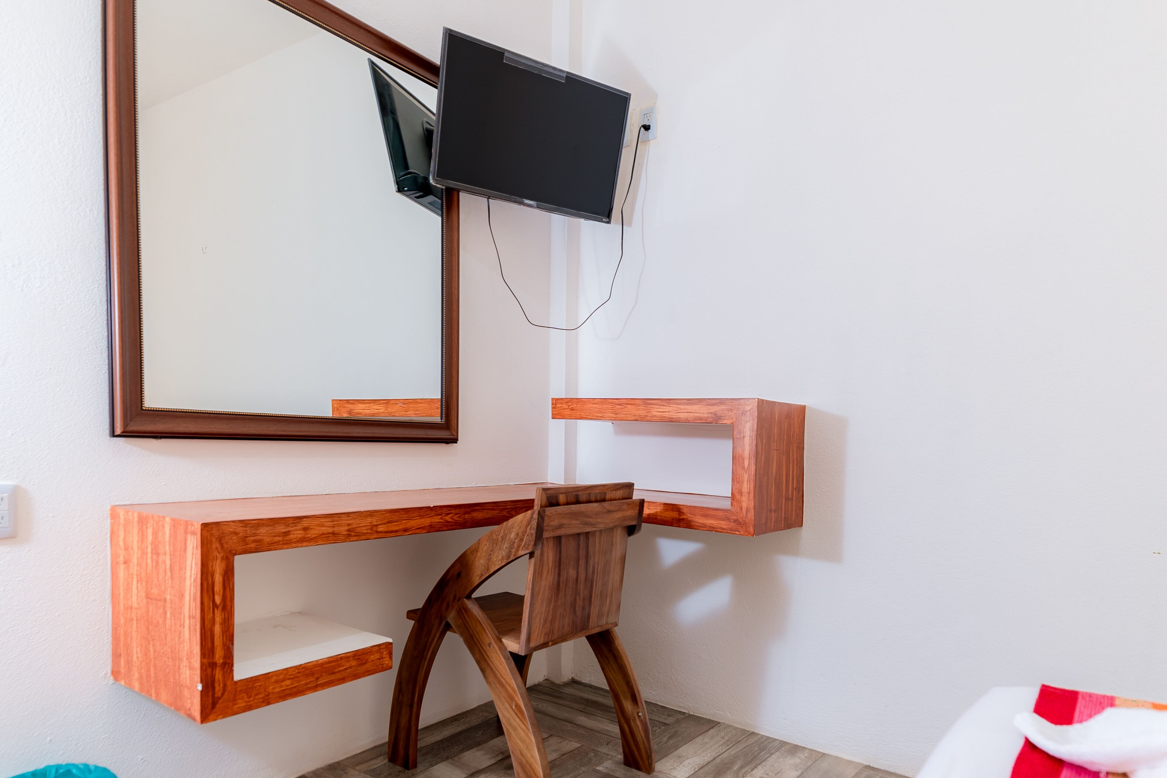 A wooden desk with a television mounted above it, a mirror on the wall, and a chair.