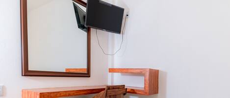 A wooden desk with a television mounted above it, a mirror on the wall, and a chair.