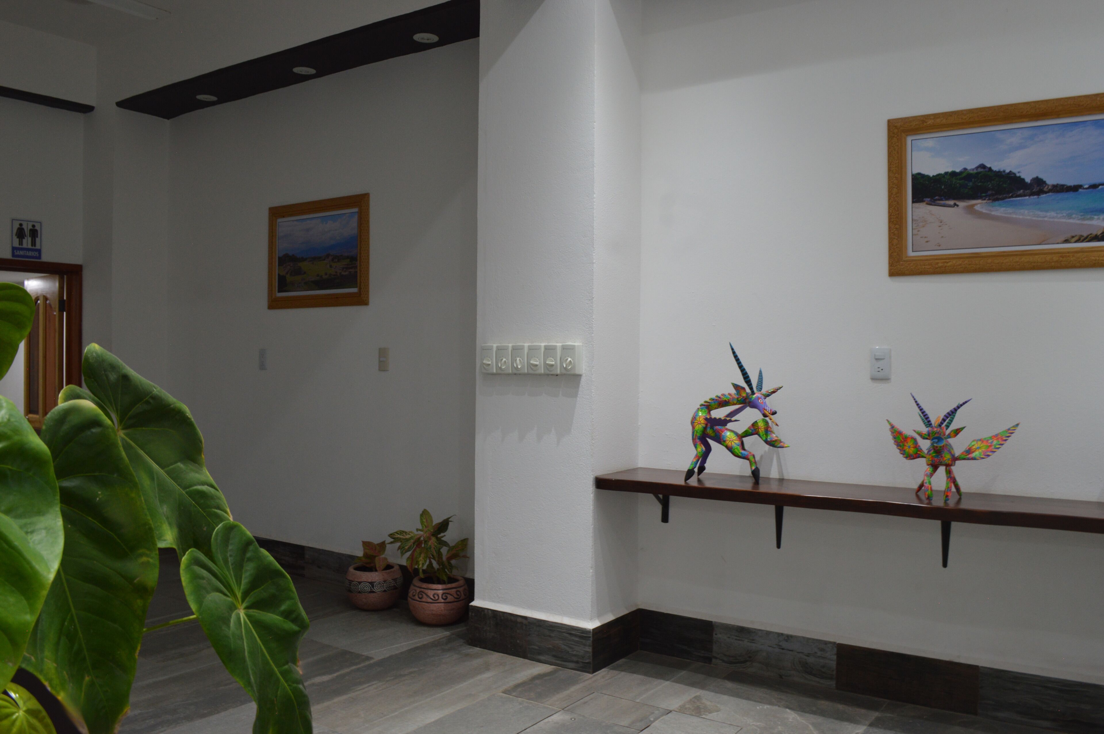 A hallway with a wooden bench, potted plants, and a framed painting on the wall.