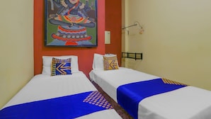 Une chambre d’hôtel avec deux lits, chacun agrémenté de draps blancs et de touches de couleur bleue, une peinture colorée au-dessus des lits et un luminaire fixé au mur.