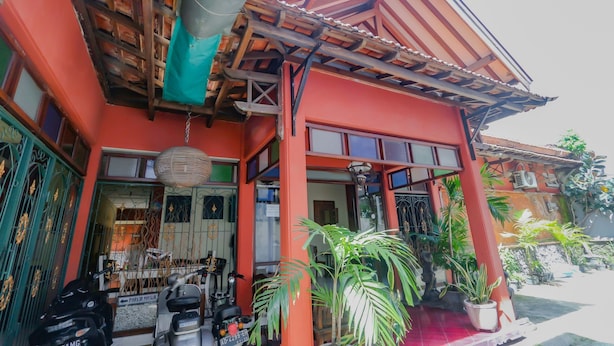 Un bâtiment rouge avec un porche abrité, des plantes en pot et des motos garées.