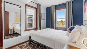 Ein Schlafzimmer mit einem Bett, einem Nachttisch, einem Spiegel und zwei Vorhängen an den Fenstern.