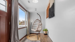 Ein Zimmer mit Holzboden, einem Hängekorbstuhl, einem runden Spiegel und einer Pflanze.