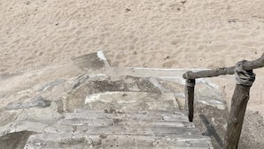 En trætrap fører ned til en sandstrand med udsigt over havet.
